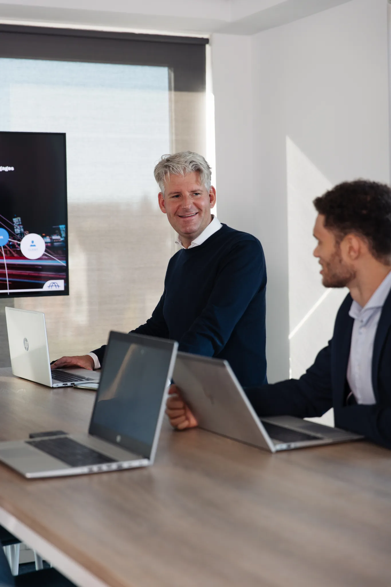 2 men looking at eachother in a conferenceroom sitting behind laptop in a conferenceroom